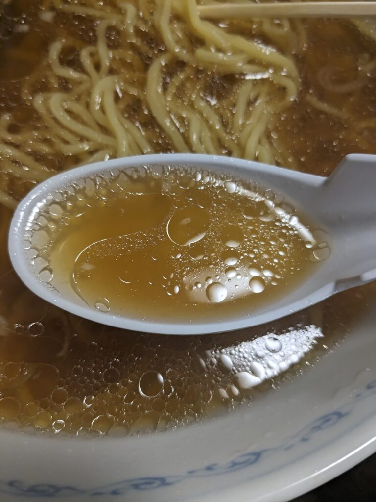 前田家の醤油ラーメンのスープをレンゲですくった様子。黄金色のあっさりスープ