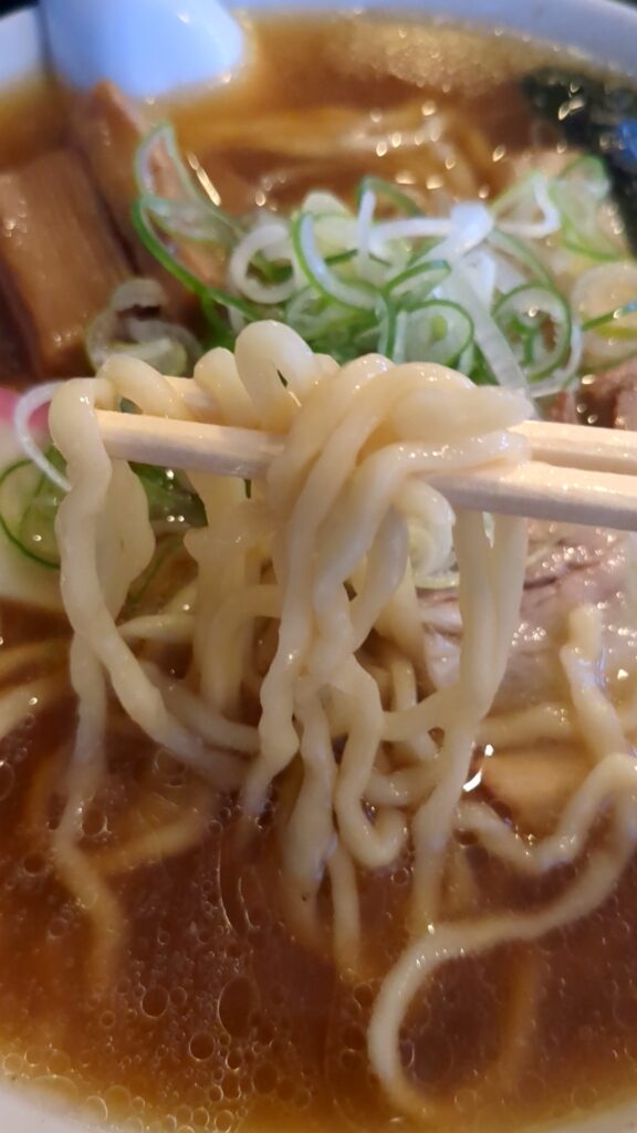 麺辰の中華そばの中太ちぢれ麺を箸で持ち上げたアップ写真。モチモチ食感の自家製麺がスープと絡む様子