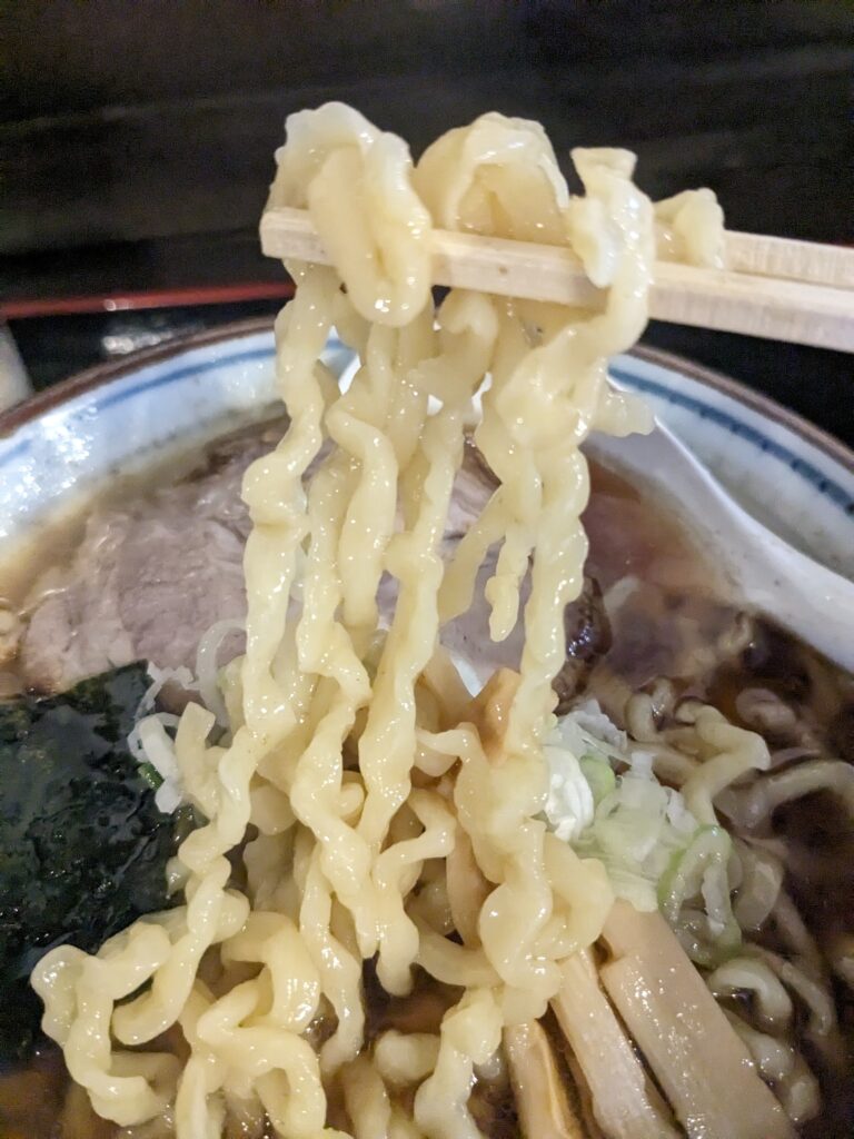 中華そばの中太ちぢれ麺を箸で持ち上げた様子。ぷりぷり感が際立っている。