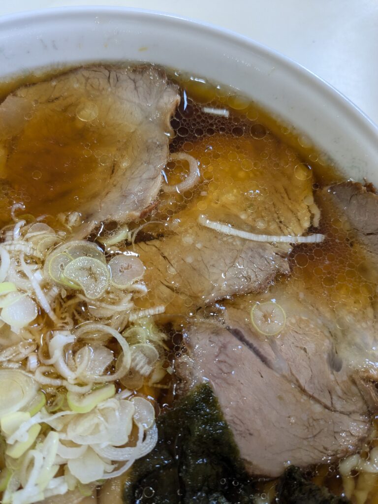 城西金ちゃんラーメンの中華そばのチャーシューとネギのアップ写真。澄んだスープに浮かぶ脂と具材が見える