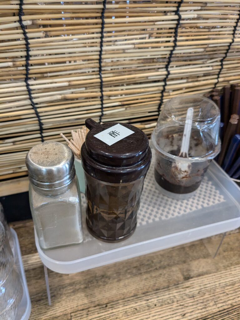 店内の卓上に並ぶ調味料。酢や胡椒、調味味噌らしきものが置かれている。