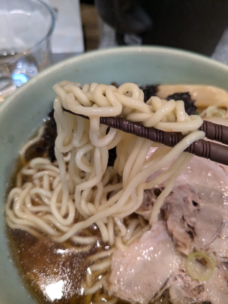 箸で持ち上げた中細ストレート麺の様子。スープの絡みが良い。